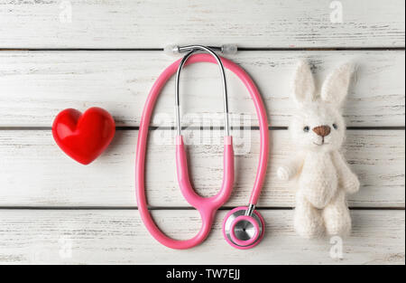 Mignon lapin tricoté, petit cœur et stéthoscope sur fond de bois blanc. Concept de visiter le médecin de l'enfant Banque D'Images