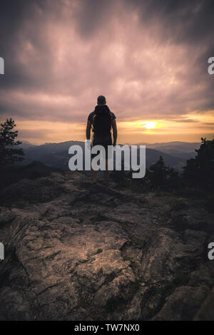 L'homme silhouette rester sur les pic. Répondre à profiter de la vue. randonneur Homme de grande taille sur une falaise rocheuse de regarder vers le bas pour le paysage pendant le coucher du soleil Banque D'Images