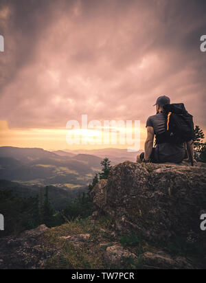 L'homme silhouette rester sur les pic. Répondre à profiter de la vue. randonneur Homme de grande taille sur une falaise rocheuse de regarder vers le bas pour le paysage pendant le coucher du soleil Banque D'Images