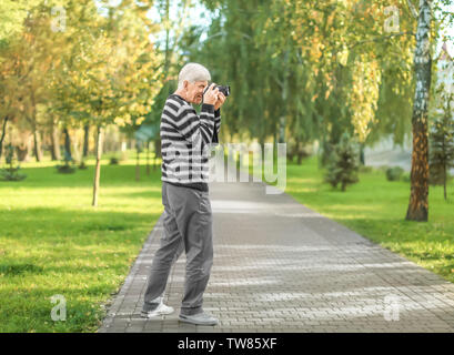 Homme mûr élégant taking photo in autumn park Banque D'Images