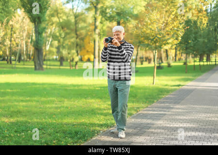 Homme mûr élégant taking photo in autumn park Banque D'Images
