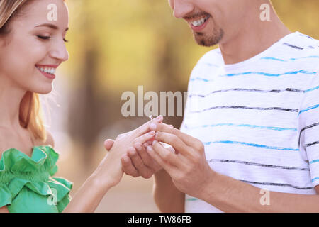 Young man putting bague de fiançailles sur fiancee's finger in park Banque D'Images