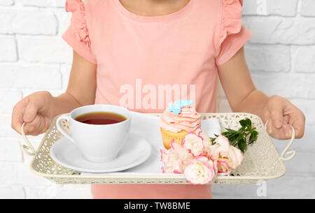 Little girl holding tray with breakfast et des fleurs pour sa maman le jour de la mère contre un mur de briques Banque D'Images