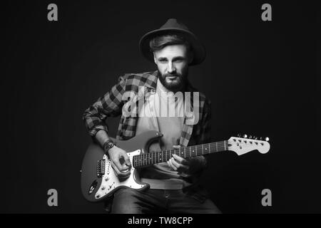 Beau jeune musicien qui joue de la guitare sur fond noir Banque D'Images