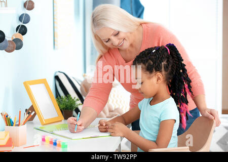 Mature nanny aidant les petits fille afro-américaine pour faire ses devoirs Banque D'Images