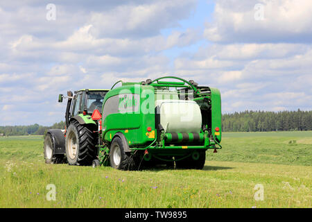 Salo, Finlande. Le 15 juin 2019. Tracteur Deutz-Fahr et McHale 3 plus l'ensilage en balles en plastique vert feuille dans champ de foin sur une journée ensoleillée d'été. Banque D'Images