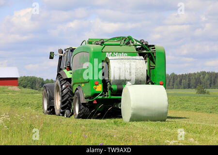 Salo, Finlande. Le 15 juin 2019. Tracteur Deutz-Fahr et McHale 3 plus l'ensilage en balles en plastique vert feuille dans champ de foin sur une journée ensoleillée d'été. Banque D'Images