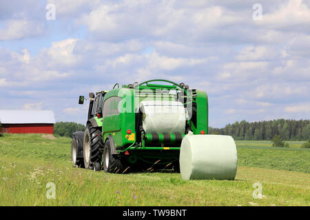 Salo, Finlande. Le 15 juin 2019. Tracteur Deutz-Fahr et McHale 3 plus l'ensilage en balles en plastique vert feuille dans champ de foin sur une journée ensoleillée d'été. Banque D'Images