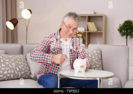 Mature man holding hammer plus de tirelire à la maison Banque D'Images