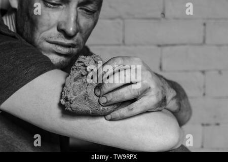 Pauvre homme affamé avec morceau de pain près de brick wall Banque D'Images