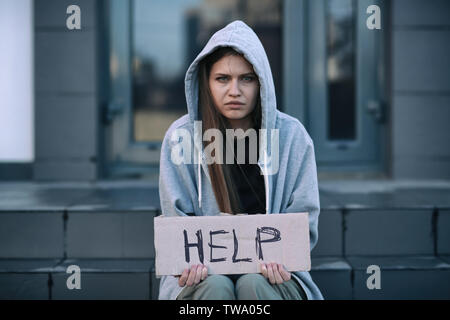 Pauvre femme sans-abri holding morceau de carton avec word aide à l'extérieur Banque D'Images