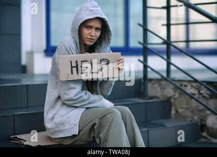 Pauvre femme sans-abri holding morceau de carton avec word aide à l'extérieur Banque D'Images