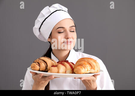Belle femme chef maintenant la plaque avec les croissants sur fond gris Banque D'Images