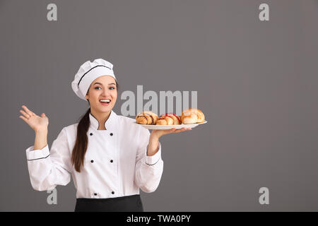 Belle femme chef maintenant la plaque avec les croissants sur fond gris Banque D'Images