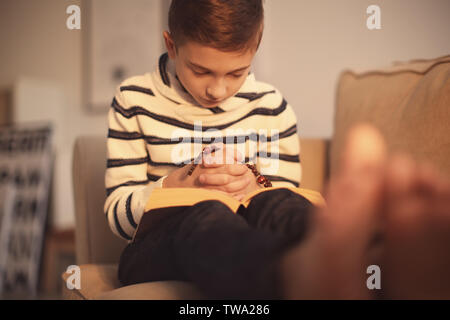 Petit garçon priant sur canapé à l'intérieur Banque D'Images