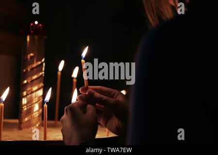 Femme allumant bougie sur fond sombre. La religion chrétienne Banque D'Images