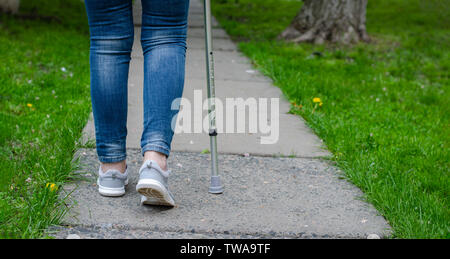 Senior woman in jeans marche avec canne à l'extérieur. Concept de réhabilitation et de redressement. Copy space Banque D'Images