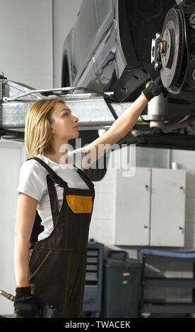 Vue de côté de belle femme en polyester et de protection à la voiture de location à Tyr dans le service automobile. Mécanicien professionnel de la réparation des véhicules endommagés dans la fixation et l'atelier. Concept d'entretien. Banque D'Images