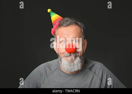 Homme mûr dans drôle déguisement sur fond sombre. April fool's day celebration Banque D'Images