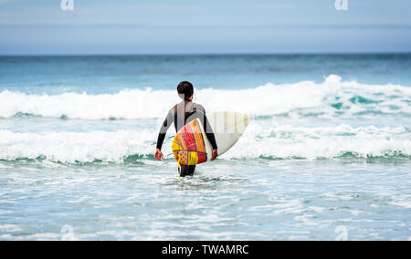 Guy with surfboard surfeur dans la main en courant vers les grosses vagues. L'homme en combinaison de surf est en marche dans les vagues de froid de l'océan atlantique en Galice, Espagne. Banque D'Images