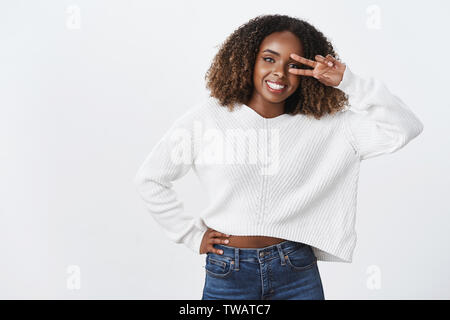 Friendly africains-américains charmante jeune fille potelée victoire afficher près de geste de paix eye smiling sont heureusement meilleure journée l'humeur positive blanc permanent Banque D'Images