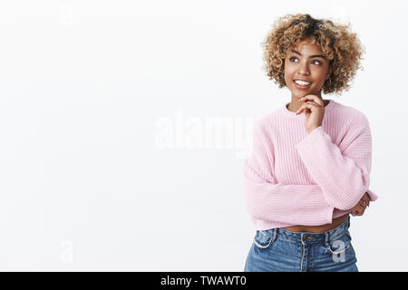 Séduisant jeune étudiante afro-américaine aux cheveux blonds tenant la main sur le menton et à heureux dans le coin en haut à gauche comme la pensée, posing Banque D'Images