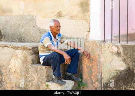 Un vieil homme cubain avoir une cigarette assis sur des pas dans la rue à Trinidad, Cuba. Banque D'Images