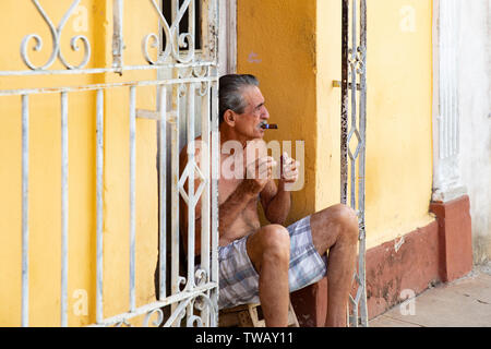 Un homme fumant un cigare cubain assis sur quelques mesures à l'extérieur de sa maison à Trinidad, Cuba. Banque D'Images