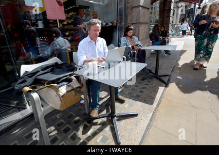 Londres, Angleterre, Royaume-Uni. Les gens assis à l'extérieur de cafe tables dans Piccadilly. L'homme sur son ordinateur portable Banque D'Images