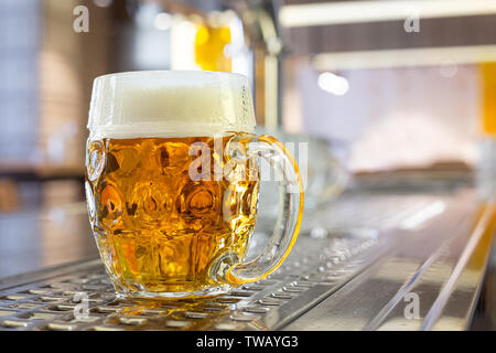 Projet de la bière fraîchement coulé dans une tasse en verre alvéolée sur comptoir en acier inoxydable dans un pub moderne. L'espace pour le texte. Banque D'Images