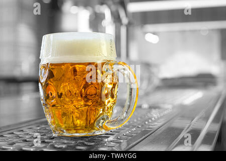 Projet de la bière fraîchement coulé dans une tasse en verre alvéolée sur comptoir en acier inoxydable dans un pub moderne. Fond noir et blanc. L'espace pour le texte. Banque D'Images