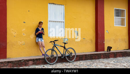 Une dame cubaine appuyé contre un mur en décomposition pendant le contrôle son téléphone portable à côté de son vélo dans la région de Sancti Spiritus, Cuba Banque D'Images
