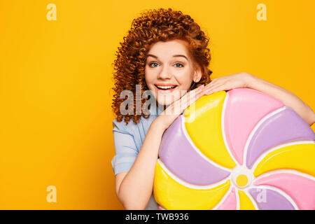 Rousse bouclée femme positive portant robe bleue avec sweet big lollipop sur fond jaune Banque D'Images