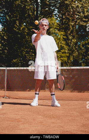Sport Tennis. L'homme jouant au tennis en plein air. Portrait Of Attractive Young Man In White T-shirt avec Raquette et balle sur fond de ciel. Mode de vie actif Banque D'Images