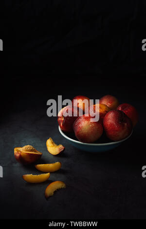 Still Life of fresh delicious sweet nectarines avec des gouttelettes d'eau dans un bol sur fond sombre. Clé faible. Banque D'Images