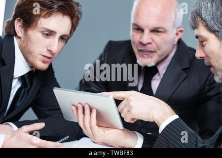 Trois hommes d'avoir une équipe motivée réunion à discuter de l'information sur une tablette ou mobile avec les expressions grossoyée Banque D'Images