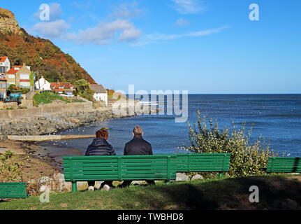 Un couple assis sur un banc vert, à la SAE Nord à Runswick Bay, North Yorkshire, UK. Banque D'Images