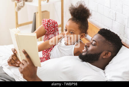 Bedtime Story. Cute girl africaine à l'écoute de conte de fées, père de la lecture livre à son enfant à la Chambre, d'espace libre Banque D'Images