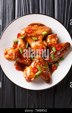 Les ailes de poulet dans la sauce teriyaki servi avec des oignons et piment, close-up sur une plaque sur la table. Haut Vertical Vue de dessus Banque D'Images