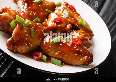 Les ailes de poulet dans la sauce teriyaki servi avec des oignons et piment, close-up sur une plaque sur la table horizontale. Banque D'Images