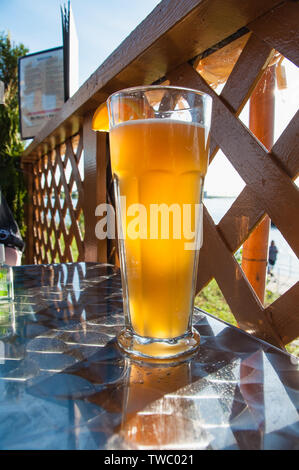 La lumière du soleil qui brillait à travers un verre de bière glacée avec un filtre orange sur le bord assis sur une table en métal à côté d'une clôture en treillis Banque D'Images