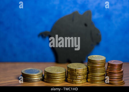 Une tirelire en carton noir et d'une pile de pièces d'euros dans un fond bleu Banque D'Images