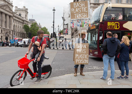 Les cycles d'un père regarde un manifestant des plastiques alors que sur un vélo de location et porte son enfant sur un harnais poitrine à la place du Parlement, Westminster, le 18 juin 2019, à Londres, en Angleterre. Banque D'Images