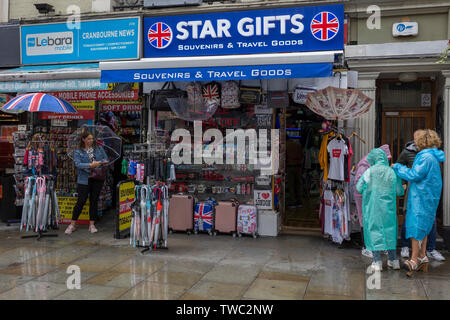 En tant que femme protège sous son parapluie, une famille touristique mis sur les Mac de pluie en plastique en face d'une boutique de souvenirs vendant des cadeaux voyage au centre de Londres, le 15 juin 2019, à Londres, en Angleterre. Banque D'Images