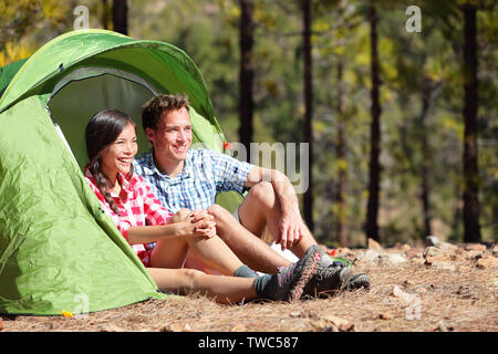 Camping en tente couple assis à la recherche à vue dans la forêt. Les campeurs smiling happy en plein air dans la forêt. Heureux couple multiracial relaxant après activité de plein air. Asian Woman, man. Banque D'Images