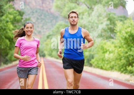 Deux coureurs dans la course à l'exercice à l'extérieur sur la route dans la belle nature de la formation de marathon. Sports multiraciale, couple modèle sport femme asiatique homme modèle de remise en forme et l'exercice de smiling happy. Banque D'Images