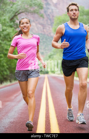 L'exécution de personnes - deux coureurs du jogging sur route dans la belle nature de la formation de marathon. Sports multiraciale, couple modèle sport femme asiatique homme modèle de remise en forme et l'exercice ensemble souriant heureux. Banque D'Images