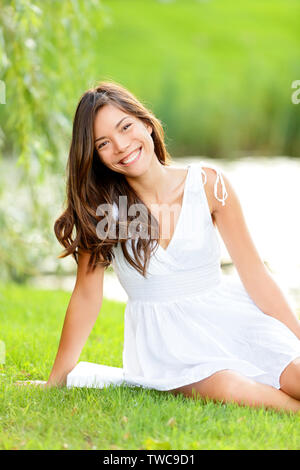 Brunette woman in summer park. Belle mixed race woman asiatiques avec de beaux cheveux longs brun assis dans un parc à l'extérieur regardant la caméra. Banque D'Images