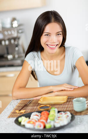 Sushi style de vie sain. Jolie métisse jeune modèle féminin assis à table à l'intérieur avec plaque sushi - à propos de manger, sourire heureux. Banque D'Images