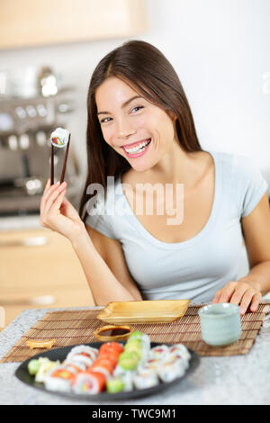 Maki sushi. Mode de vie sain femme sur le point de manger des sushis. Mixed Race pretty young woman holding chopsticks smiling heureusement et joyeux. En face de la plaque sushi complet Banque D'Images